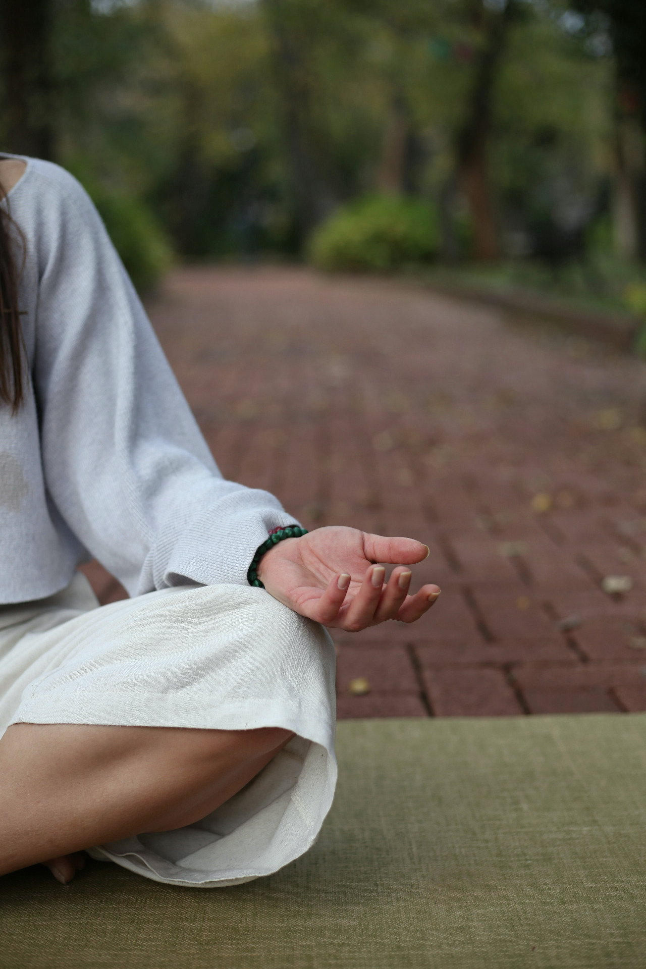 Copyright Cansu Hangul on Unsplash. Bildet viser venstre del av en skikkelse kledd i hvit som sitter i skredderstilling på en yogamatte på bakken med hendene på fanget og håndflatene vendt mot himelen